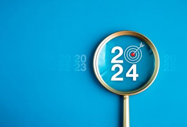 İş konsepti afişiyle 2024 yılınız kutlu olsun. Açık mavi arka planda altın büyüteçin içinde hedef ikon bulunan büyük beyaz 2024 yılı numarası. Hedef ve başarı kavramları için planlama.