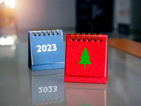 Merry Christmas day calendar with green Christmas tree minimal graphic icon on red folding desk calendar standing and 2023 numbers on table in workplace. Xmas holiday party date reminder concept.