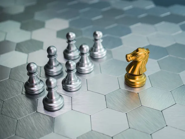 The golden Horse, knight chess piece standing in front of silver pawn pieces on silver hexagon pattern board background. Leadership, follower, team, commander, competition, business strategy concept.