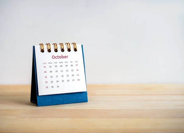 An October 2023 calendar desk for the organizer to plan and reminder isolated on wood table and white background with copy space, minimal style. Blue small table calendar with page of the 10th month.