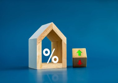 Ev vergisi kavramı. İkamet oranı, gayrimenkul, mülk ve yıllık vergilendirme. Modern beyaz ahşap ev modelinde büyük bir yüzdelik simge ve mavi arka planda tahta blokta yukarı aşağı ok..