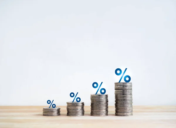 Blue percentage icon on coin stacked as a bar graph chart steps isolated on wood table, white background. Investment, profit, benefit, income, banking, business growth, economic improvement concepts.