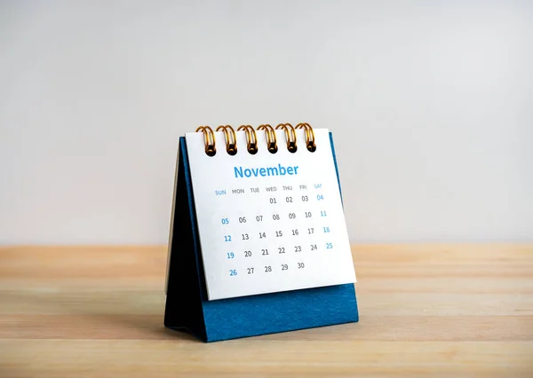 An November 2023 calendar desk for the organizer to plan and reminder isolated on wood table and white background, minimal style. Blue small table calendar with page of the 11th month.