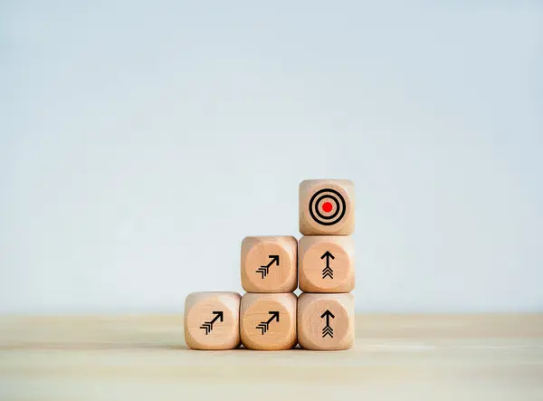 Goal target icon and towards arrows symbol on wooden cube blocks as business graph steps on desk, white background. Business growth process, objective goals, dashing to the target, success concepts.