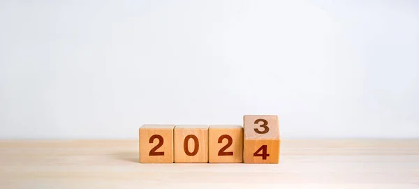 2024 happy new year with change to new era concepts. Flipping the 2023 to 2024 year calendar numbers on wooden cube blocks isolated on wood table and white banner background, minimalist simple style.