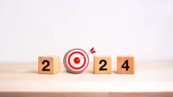 2024 business goal and success concept banner. Text, year number on wooden cube block with 3d target dart icon on wood table and white background. Welcome, Merry Christmas, and Happy New Year in 2024.