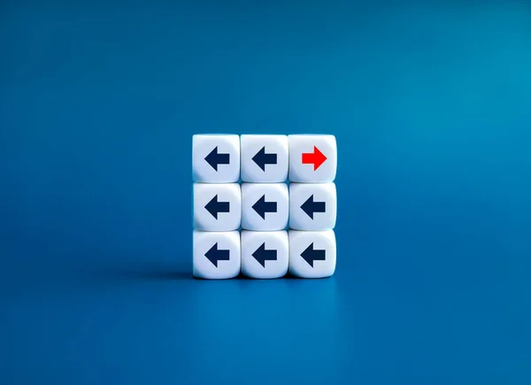 Leadership, opposite, disrupt, unique, think different way and stand out from the crowd concepts. Red go right and black go left, arrow direction symbol on white dice blocks on blue background.
