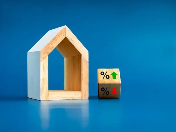 Home tax concept. Resident rate, real estate, property and building annual taxation. Percentage icon and up and down arrow on flip wood block near modern wooden white house model on blue background.