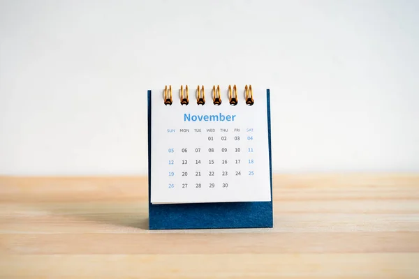 An November 2023 calendar desk for the organizer to plan and reminder isolated on wood table and white background, minimal style. Front view of blue small table calendar with page of the 11th month.