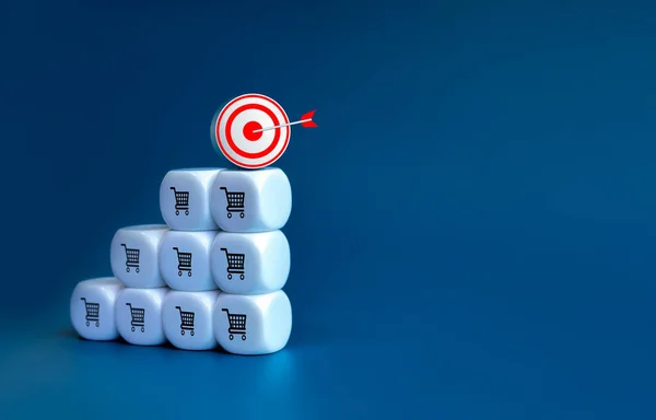 3d Target icon on top of white cube block stack as a growth graph steps with shopping cart icons on blue background with copy space. Business growth, sales increase and profit income concept.