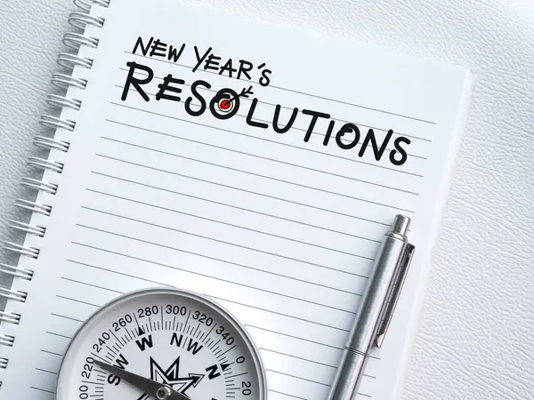 Goals, action, plan, business direction and to do list concepts in new year. Handwriting text, NEW YEAR\'S RESOLUTIONS with target icon, pen and compass on white notebook page background with space.