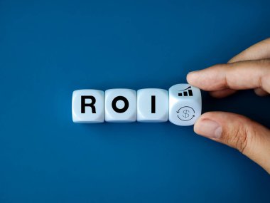 ROI, Yatırımın Dönüşü, pasif gelir, iş gelirleri kavramları. Blokları ROI ile el ele çevirmede büyüme grafiği simgesi ve tiraj para sembolü, mavi arkaplanda beyaz küp bloklar üzerine metin.