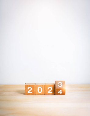 2024 mutlu yıllar ve yeni dönem kavramları. Ahşap masa üzerinde izole edilmiş tahta küp bloklardaki 2023 'ten 2024' e kadar olan takvim numaralarını çevirmek ve beyaz dikey afiş arkaplanı, asgari biçim.