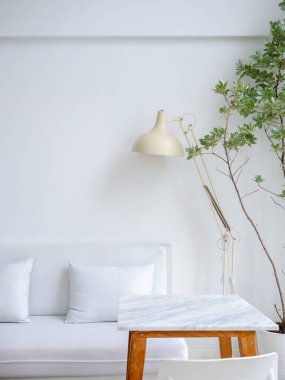 Modern dinlenme ve temiz oturma odası dekorasyonu beyaz kanepe ya da yastıklı kanepe, bej masa lambası boş mermer masa ve yeşil yapraklar, ev bitkisi, dikey stil.