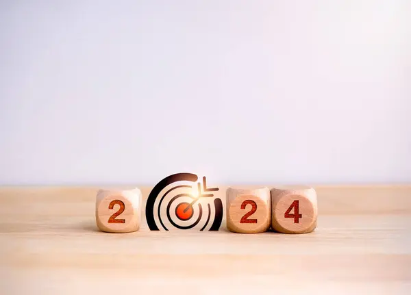 Happy 2024 calendar year with goal and success concepts. Big target dart icon and 2024 year number on wooden cube block isolated on desk, white background. Happy new year, big business goals banner.