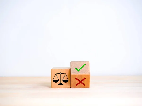 Decision, right or wrong, moral issue, ethical dilemma concepts. Scales of justice, icon on wood cube near green check mark and red cross symbol on flipping wooden block on table and white background.