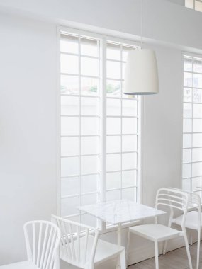 Tavandan sarkan modern yuvarlak lamba silindirik şekilli boş masa ve parlak kafe veya restoranda uzun pencere ızgarası tarzında sandalyeler. Işıklı beyaz oda iç dekorasyonu.