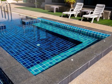 Yüzme havuzunda oturacak bir yer, temiz su, hiç kimse. Yeşil camlı çift beyaz güneş yatağının yanında mavi fayanslı kare şeklinde bir havuz, insan yok. Yaz arkaplanı.