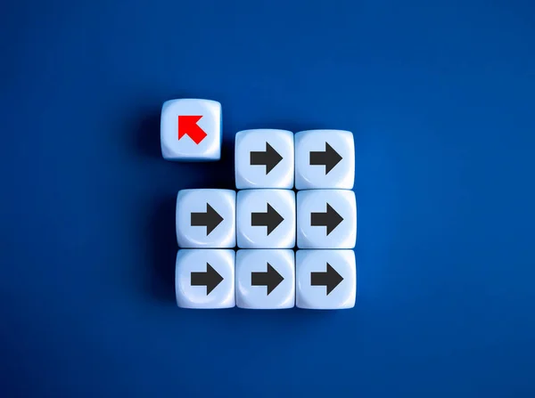 Leadership, opposite, disrupt, unique, think different way and stand out from the crowd concepts. Red arrow go out from group of right way arrow direction symbol on white dice blocks, blue background.