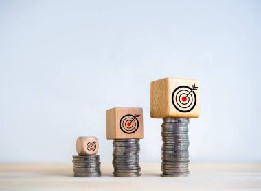 Tahta küp bloklardaki hedef simgeleri bozuk para yığını grafiğinde genişleyen beyaz zemin üzerindeki basamaklar. Yatırım, kâr, gelir, satış, iş hedefi, büyüme ve başarı, ekonomik iyileştirme kavramları.