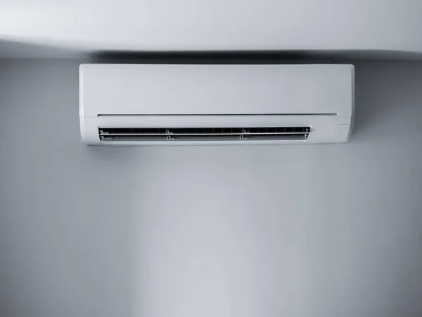 Air conditioner wall mounted decorative. Photo of white air condition hanging on clear wall background under the ceiling in empty room. Electrical wind machine equipment in house.