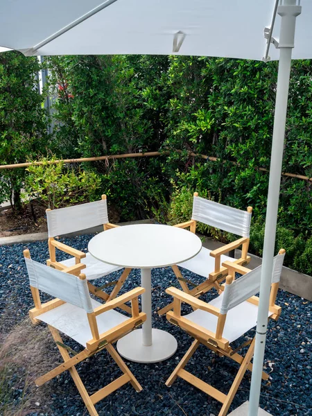 Four empty director chairs, fabric and wood materials with round shape table at outdoor garden on blue gravel stone floor in the part, vertical style. Table set relaxing loft style in the garden.