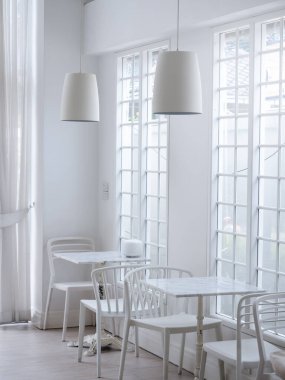 Modern yuvarlak lambalar tavandan sarkan silindirik şekilli uzun, cam pencereli, minimal oturma odası. Parlak kafe ya da restoranın masa ve sandalyeli iç dekorasyonu.