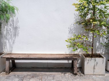 Binanın dışındaki büyük beton çömlek dekorasyonunun yanında beyaz bir duvarda kimsenin oturmadığı eski boş ahşap bank koltuğu..