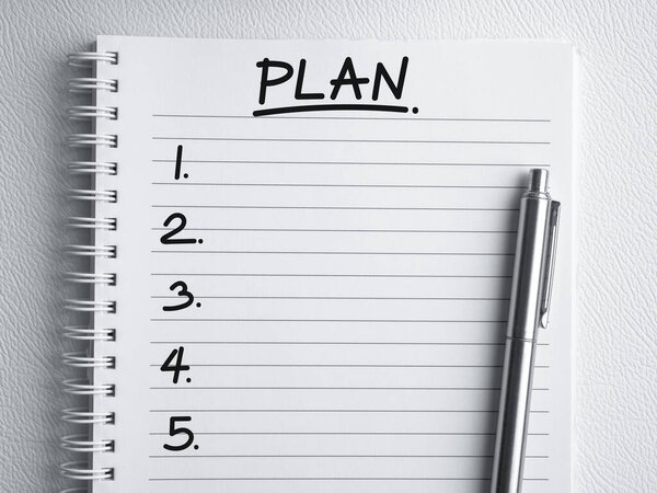 Business plan ideas, business direction and to do list concept. Handwriting text, "PLAN" with empty item 1 to 5 and pen on spiral notebook page with line, white background with copy space, top view.