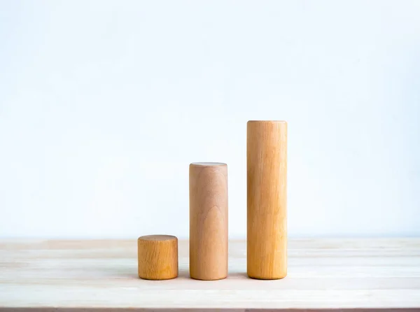 Three size of round wooden sticks as a business chart steps isolated on wood desk on white background simple style. Business growth graph process, goal, success, and economic improvement concepts.