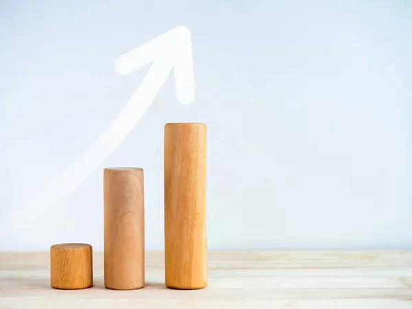 Upward arrow on round wooden sticks as business graph steps isolated on wood desk on white background with copy space. Business growth graph process, goal, success, and economic improvement concepts.