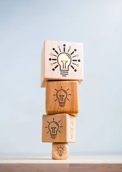 Think big. Inspiration, innovative technology, goal and success concepts. Biggest modern idea lightbulb icon on top of bulbs symbol on smaller wooden cube blocks stack isolated on white background.