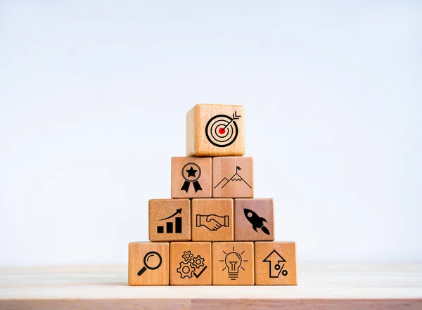 Business startup with growth success process for leadership concept. Business target plan and successful strategy icon symbols on wooden cube blocks arranged as pyramid shape on white background.