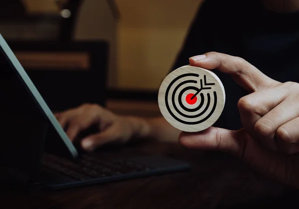 Businessman hand holding big goal, target dart icon on circle wooden while working with laptop computer. Business strategy, action plan and future innovation technology with goal and success concepts.