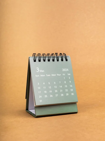 Green of March 2024 desk calendar for the organizer to plan and reminder isolated on brown craft paper background, minimal style. Small table calendar with the page of third month, vertical style.