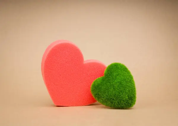 World care, earth day, eco friendly and save planet concepts. Green grass heart-shape standing together with big red heart sponge on eco brown kraft paper background for card or poster, minimalist.