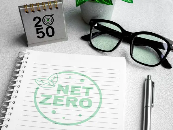 Net Zero 2050 year management plan. To do list. Net Zero icon logo on blank vertical notepad page with 2050 desk calendar, silver pen and green plant pot on white spiral notebook on white background.