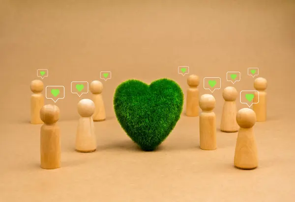 Green heart at center of community group wooden people figures with green heart, love symbol in speech bubble stand on recycled paper background. Earth care and environmental responsibility concepts.