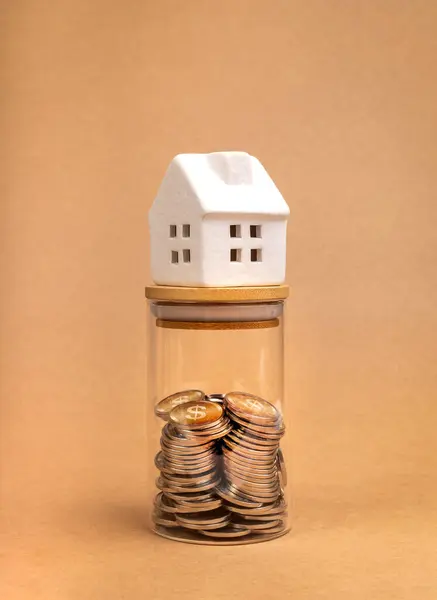 Home Tax, property investment and house mortgage financial, savings money concepts. White miniature house on glass bottle with money coins inside, isolate on recycle paper background, vertical style.