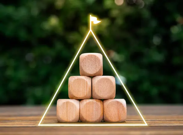 Triangle of success, business growth process, sustainable organizational concept. Glow triangle line with flag on empty blank wooden cube blocks pyramid shape on wood desk and green plant background.