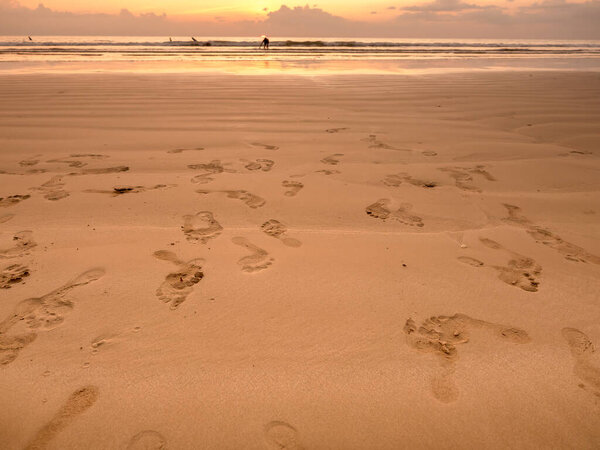 Многие оставляют следы на песчаном пляже на фоне закатного неба. Крупным планом следы многих людей с ступеньки ступеньки ходьбы разнообразным направлением на мокрый песок. Пляжные путешествия, летняя концепция.