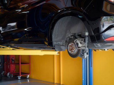 Kapalı fren diski siyah sedan arabada tekerlekleri yok. Değişiklik ya da bakım için sarı otomobil garajını ya da lastik dükkanının perakende arka planını bekleyin..