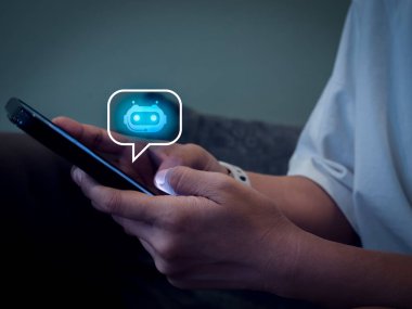 Artificial intelligence, AI chat bot technology concept. Glowing smart robot icon on speech bubble on mobile phone screen in hands, robot application and conversation assistant automation service.