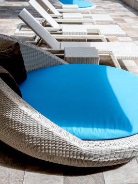 Büyük yuvarlak mavi yastıklı boş, beyaz, modern rattan koltuklar otel havuzunun havuz başındaki konuklara güneşlik koltuğu ile uzanır. Yaz yüzme havuzu rahatlama konsepti.