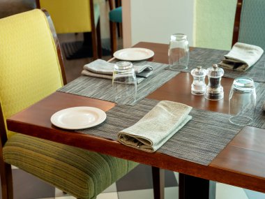 Beyaz keten peçeteler kaşık ve çatal, su bardağı ve tabak paspasları boş sandalye koltuklarının yanındaki ahşap yemek masası, konukların yemek odası veya otel odasındaki yemek için hazırlanan masa..