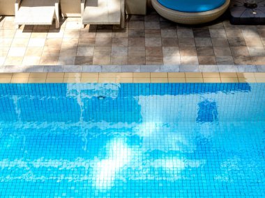 Yüzme havuzunun arka planında mavi ızgara mozaik fayanslarda, taş döşemede güneş yatağının yanında temiz su havuzu. Güneşli bir günde havuz başında boş alan, yaz arkaplanı.