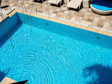 Üst görüş alanı bulanık yuvarlak su dalgalanması mavi ızgara mozaik fayanslar üzerinde yüzme havuzu arka planında, güneşli yatağın yanında hareket ediyor. Güneşli bir günde havuz başında boş alan, yaz arkaplanı.