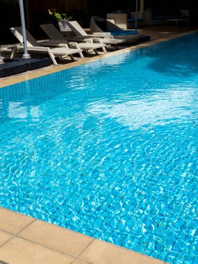 Otel için boş beyaz, modern rattan şezlonglar ya da büyük açık havuz kenarındaki ziyaretçiler için dikey bir şekilde temiz su. Yaz yüzme havuzu rahatlama konsepti.
