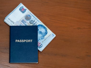 Singapur dolar para geçmişi. 50 Singapur Dolarlık banknotlu mavi pasaport, tahta masa arkaplanında, fotokopi alanı ile izole edilmiş. İş finans ve bankacılık kavramı.