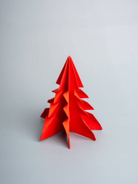 Mutlu Noeller ve mutlu yıllar konsepti, minimum stil. Gri arka planda izole edilmiş kırmızı kağıt Noel ağacı, dikey stil.